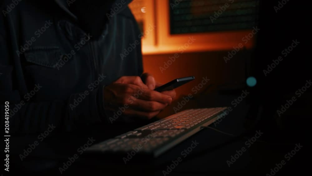 Computer hacker using smartphone in dark interior Computer hacker using smartphone in dark interior