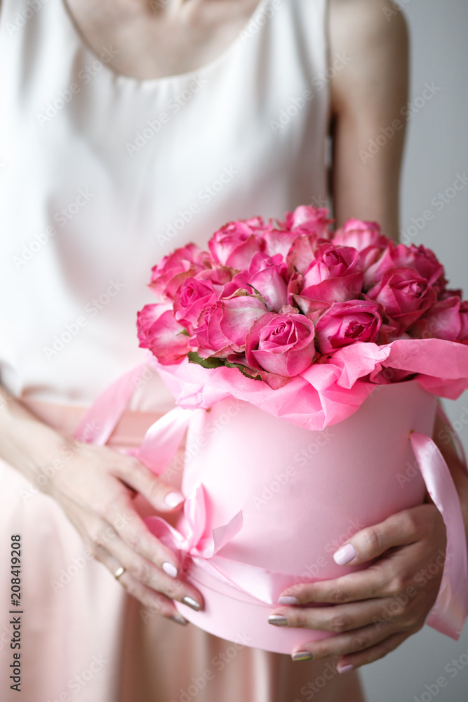 Close-up photo of gorgeous bouquet of pink roses in a hat box. Woman hands with manicure, nail polish art