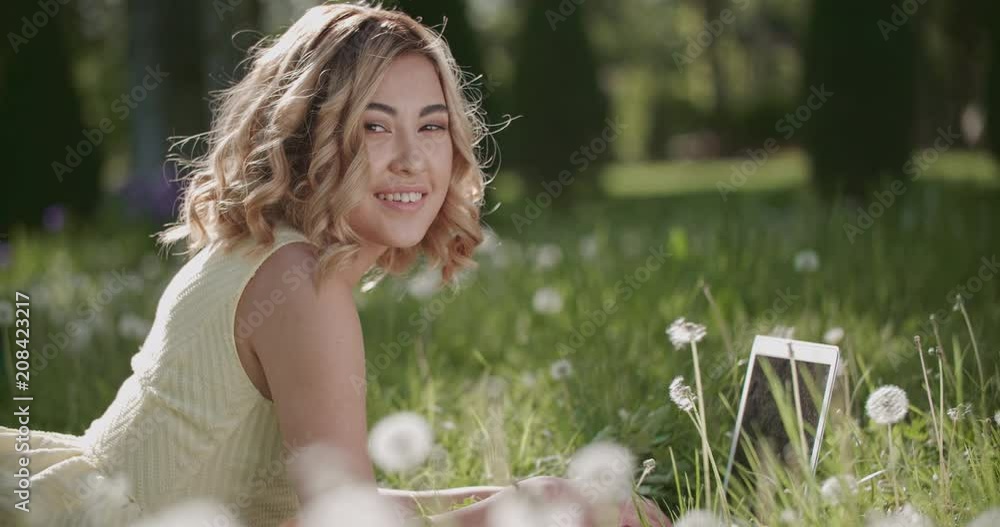 beautiful Asian girl surrounded by dandelions in the Park on a Sunny day with laptop, having fun slow motion beautiful Asian girl surrounded by dandelions in the Park on a Sunny day with laptop, having fun slow motion