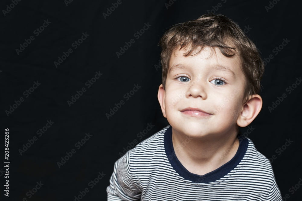 Portrait of a beautiful young boy on a black background. He smiles and raised his head up Portrait of a beautiful young boy on a black background. He smiles and raised his head up