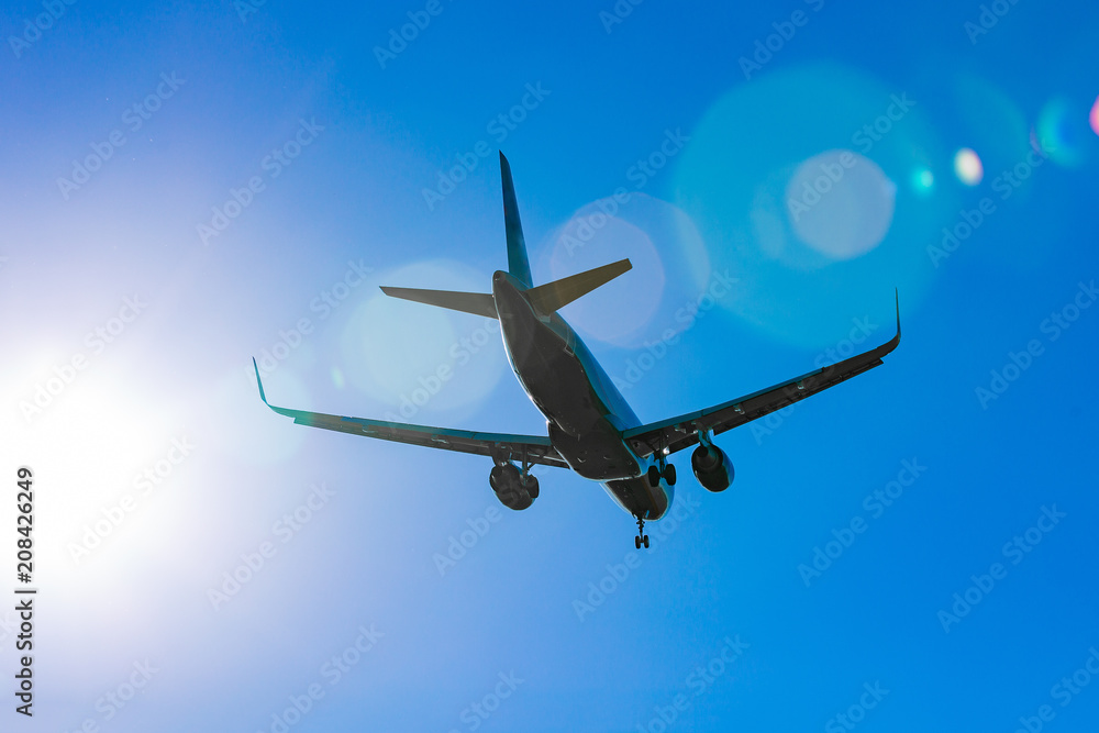 Naklejka premium Passenger plane flying in the blue sky in sunlight rays