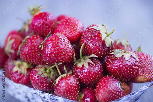 Ripe strawberries in a glass plate on a gray background.