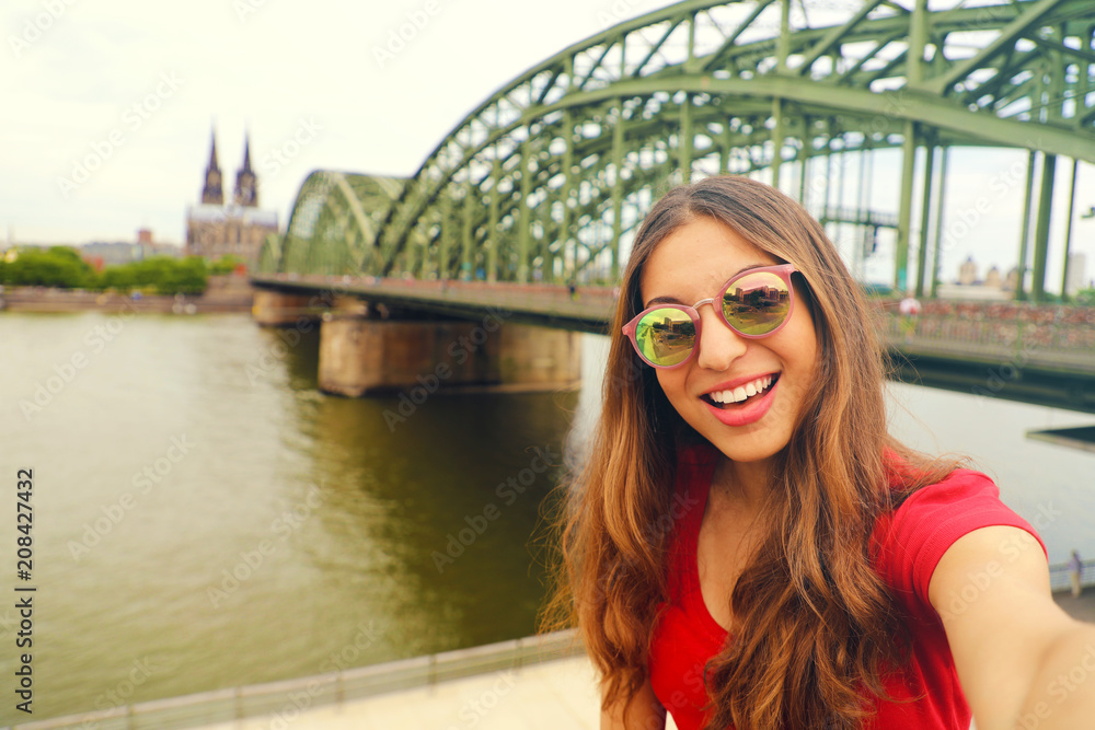 Selfie photo of young fashion woman in Cologne with Hohenzollern Bridge and Cathedral on the background, Cologne, Germany. Traveling in Europe. Vintage Filter.