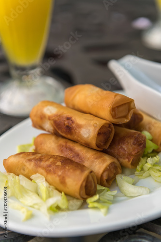 Some spring rolls stacked on each other in a salad bed. Drink in the background.