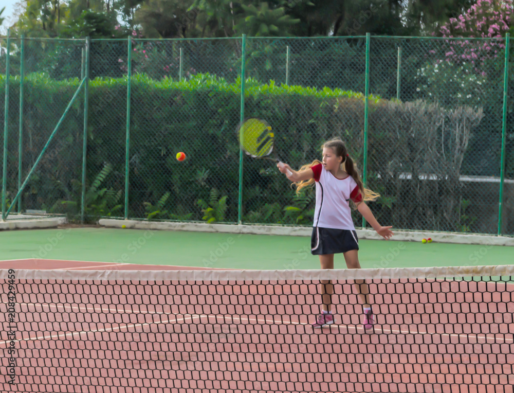 Girl tennis player, playing in the open air. Young girl playing tennis on court