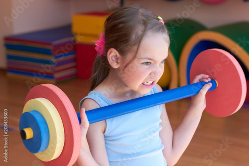 The child raises a heavy barbell in the gym.