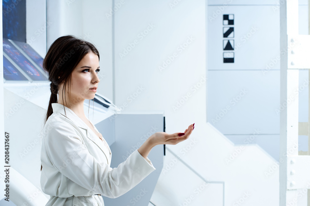Futuristic white interior reminiscent of a laboratory or a spaceship. Beautiful brunette in white clothes with blue eyes posing for the camera Futuristic white interior reminiscent of a laboratory or a spaceship. Beautiful brunette in white clothes with blue eyes posing for the camera
