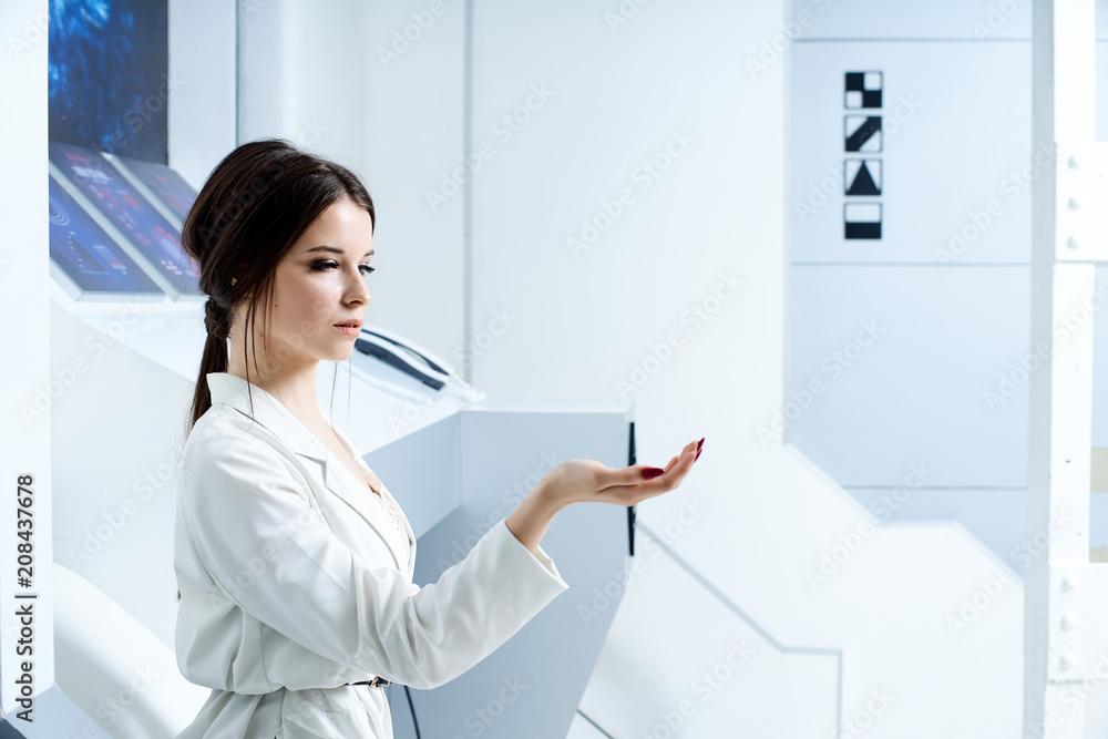 Futuristic white interior reminiscent of a laboratory or a spaceship. Beautiful brunette in white clothes with blue eyes posing for the camera Futuristic white interior reminiscent of a laboratory or a spaceship. Beautiful brunette in white clothes with blue eyes posing for the camera