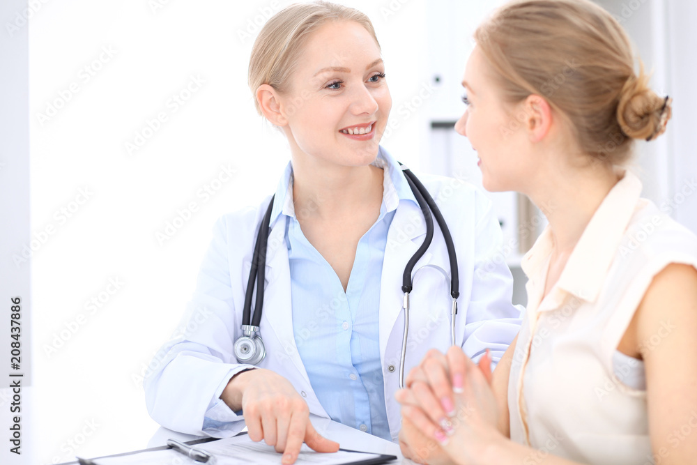 Blonde female doctor and patient talking in hospital office. Health care and client service in medicine Blonde female doctor and patient talking in hospital office. Health care and client service in medicine
