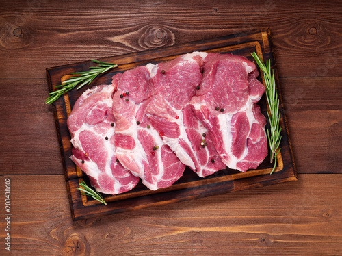 Raw Pork Loin chops on a cutting board with herbs rosemary on dark wooden background, top view