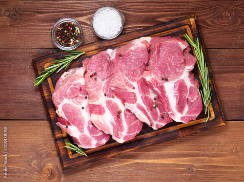 Raw Pork Loin chops on a cutting board with herbs rosemary on dark wooden background, top view