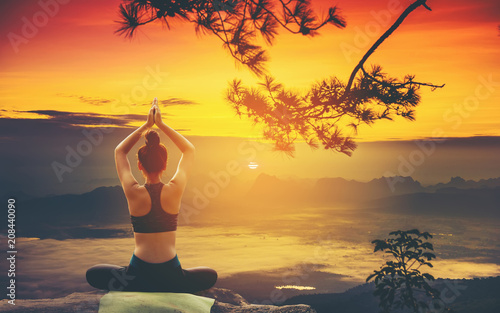 Back of Beautiful young woman practicing yoga on the high cliffs at sunrise