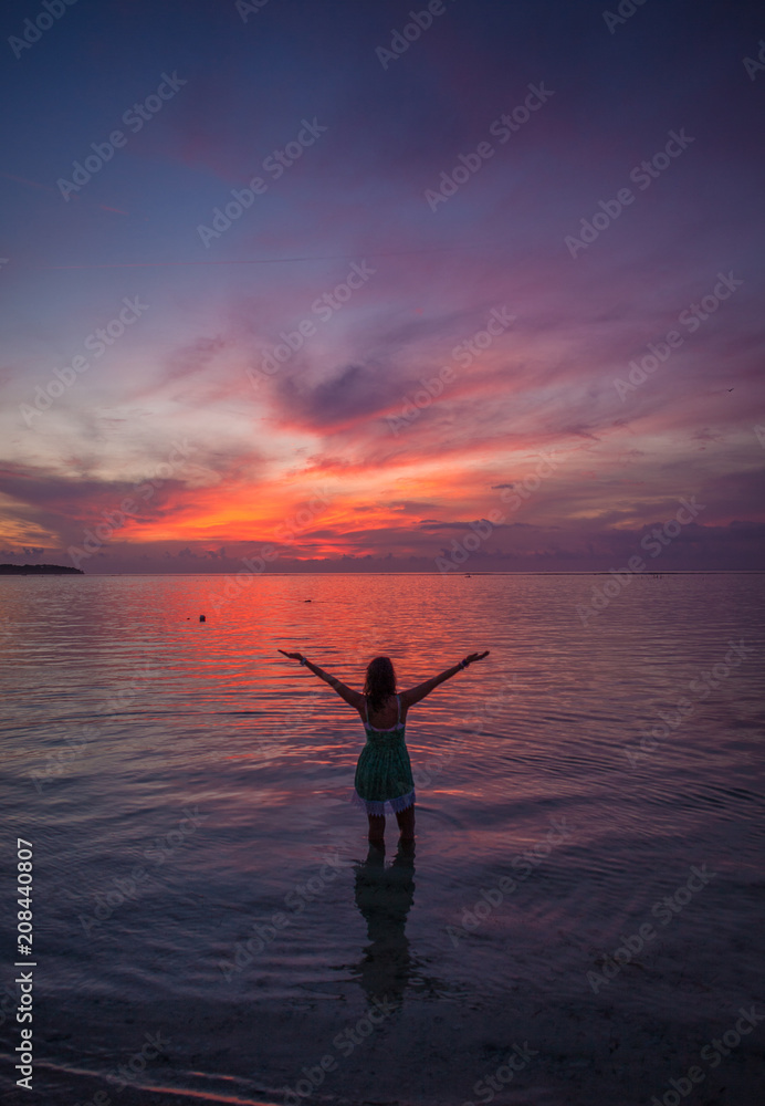 Woman at a Pink and Purple Ocean Sunset with Arms Outstretched 