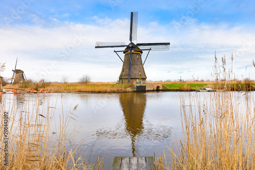Traditional Dutch windmills near the water canals with beautiful white clouds and blue sky reflecting in water. UNESCO world heritage sight in Kinderdijk, Netherlands in winter