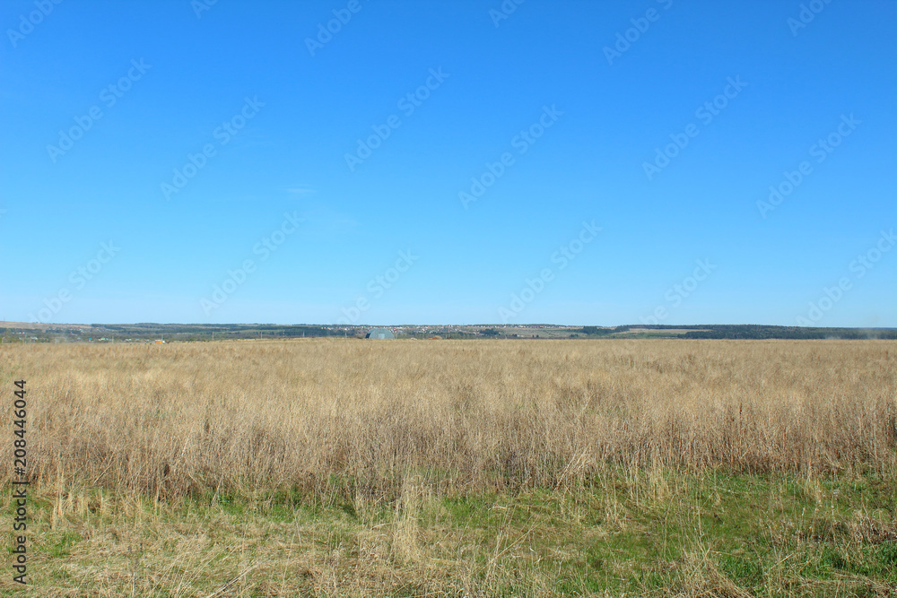 A large field with dry grass. The village is far away. Landscape. Background. May, 2018. A large field with dry grass. The village is far away. Landscape. Background. May, 2018.