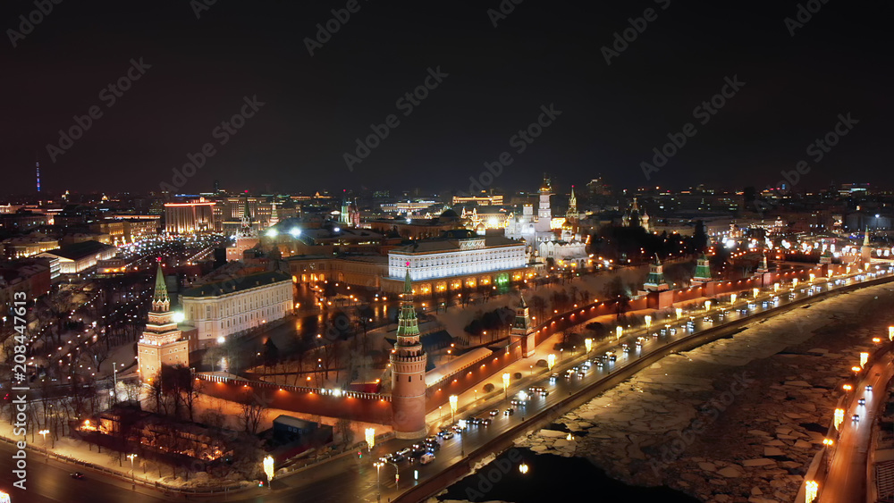 Flying above frozen river Moskva and its embankment illuminated with sparkling lanterns. Bright cityscape and Moscow Kremlin at night. Intensive traffic in the streets of Moscow.