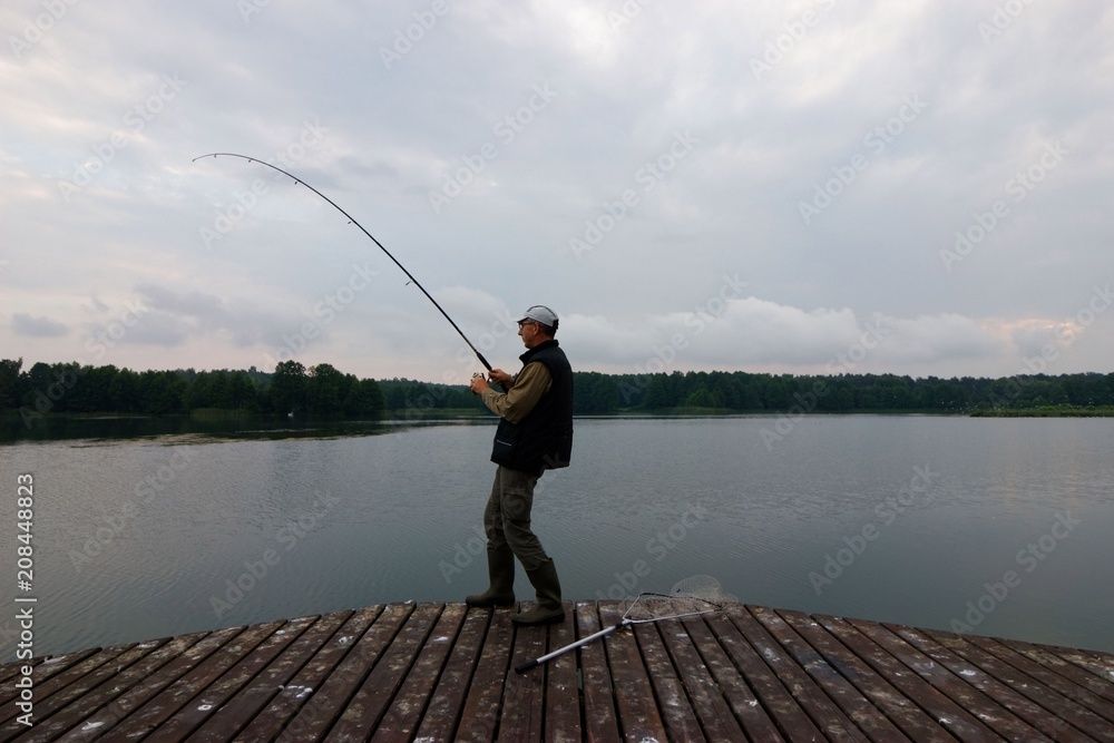 Fisherman catching the fish from wooden pier during cloudy day Fisherman catching the fish from wooden pier during cloudy day