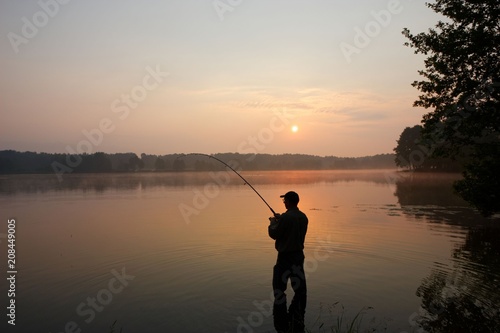 Silhouette of fisherman standing in a lake and catching the fish during sunrise
