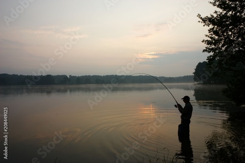 Silhouette of fisherman standing in a lake and catching the fish during sunrise