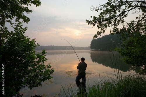 Silhouette of fisherman standing in a lake and catching the fish during sunrise © mtmmarek