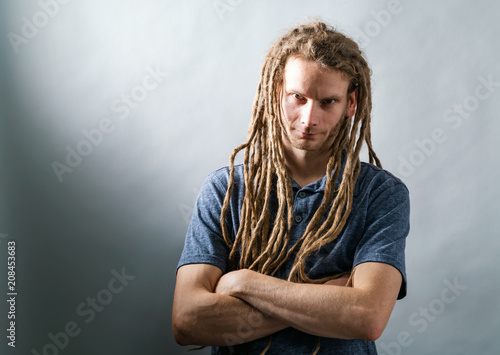 Man with dreadlocks with arms folded on a dark background