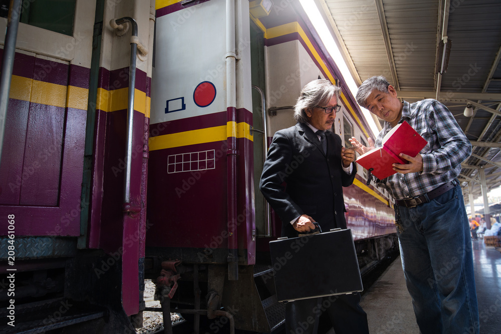 Serious Asian business men discussing information near train, both looking at the red book Serious Asian business men discussing information near train, both looking at the red book