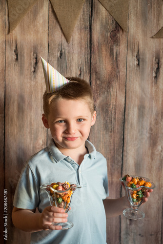 Happy joyful laughing little boy at a party. Holds a colorful popcorn in a glass. On a wooden background with flags photo