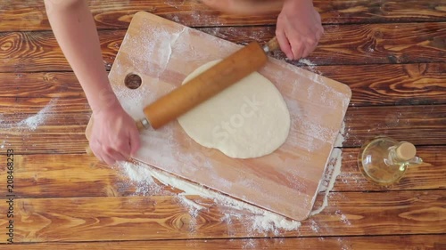 Woman's hands rolling dough on wooden board, top view video photo