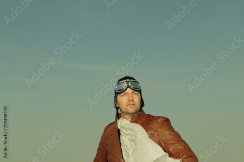 Portrait of a vintage pilot with leather cap, scarf and aviator glasses salutes - Portrait of a man in historical pilot clothing © Riko Best