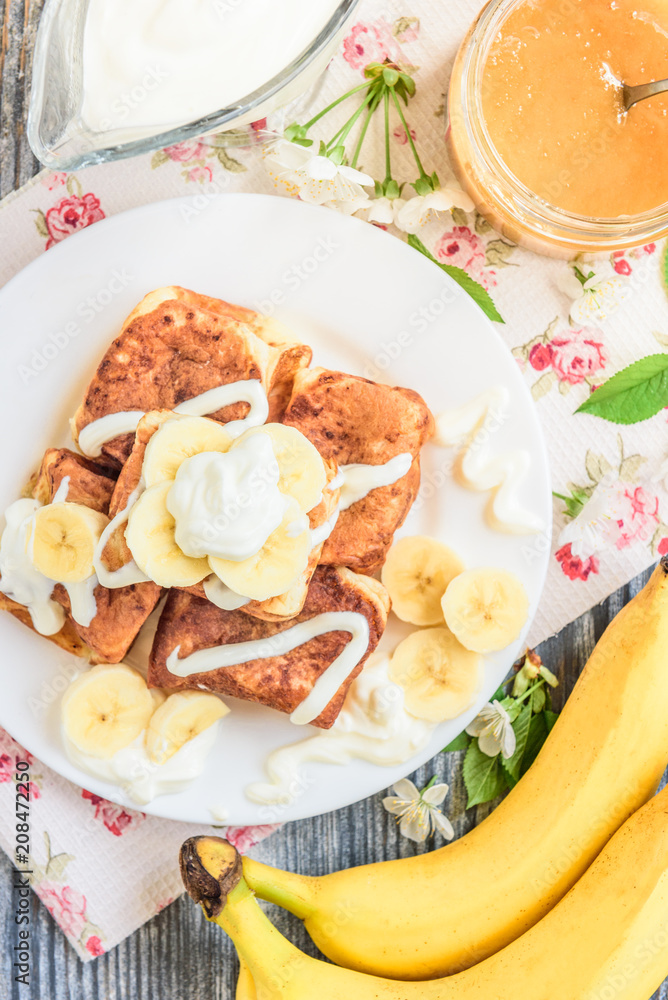 Cottage cheese pancakes in the form of cubes with banana, yogurt, honey and cherry blossom flowers on grey wooden background. Healthy breakfast food.