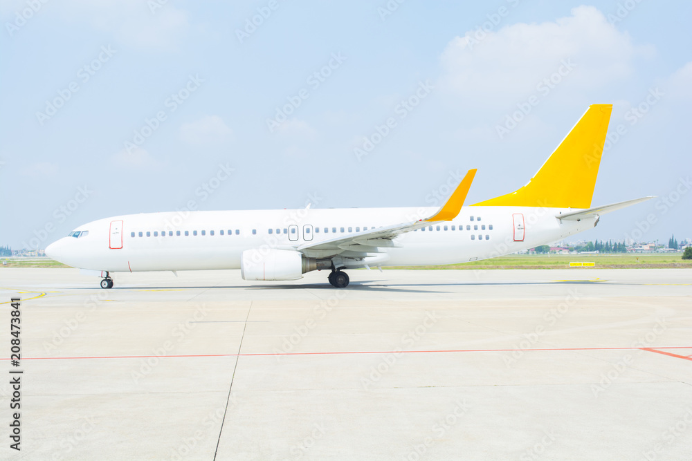 White passenger airplane on the airport runway. The plane is taking off during a could blue sky.