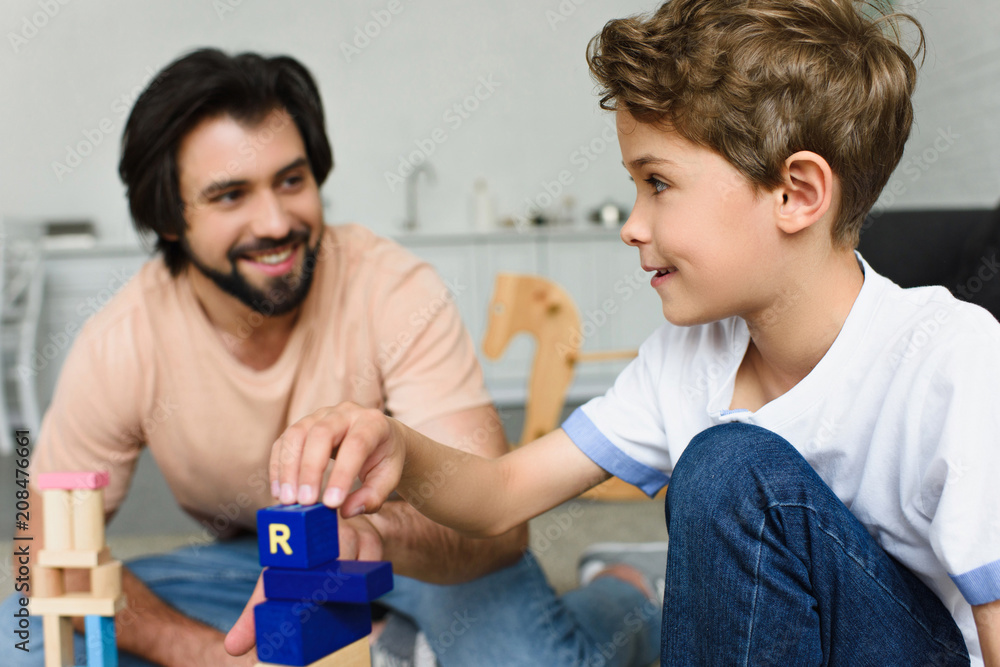 selective focus of father and son playing with wooden blocks together at home