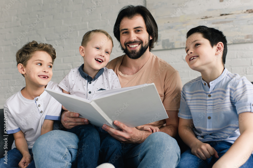 portrait of smiling father and sons reading book together at home portrait of smiling father and sons reading book together at home