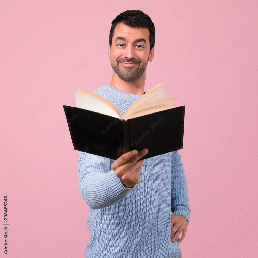 Man with blue sweater holding and reading a book on pink background Man with blue sweater holding and reading a book on pink background