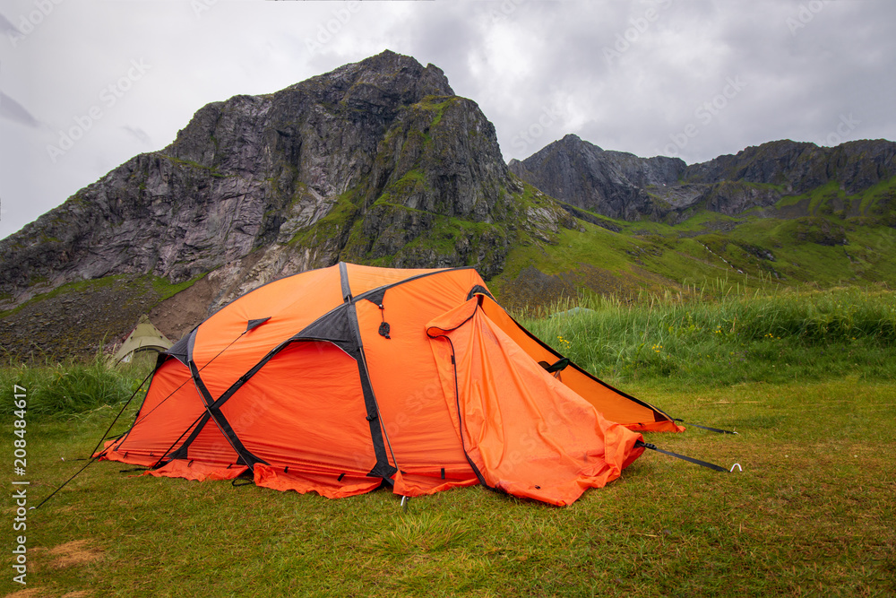 oranges Zelt auf einer Wiese vor den Bergen, Lofoten