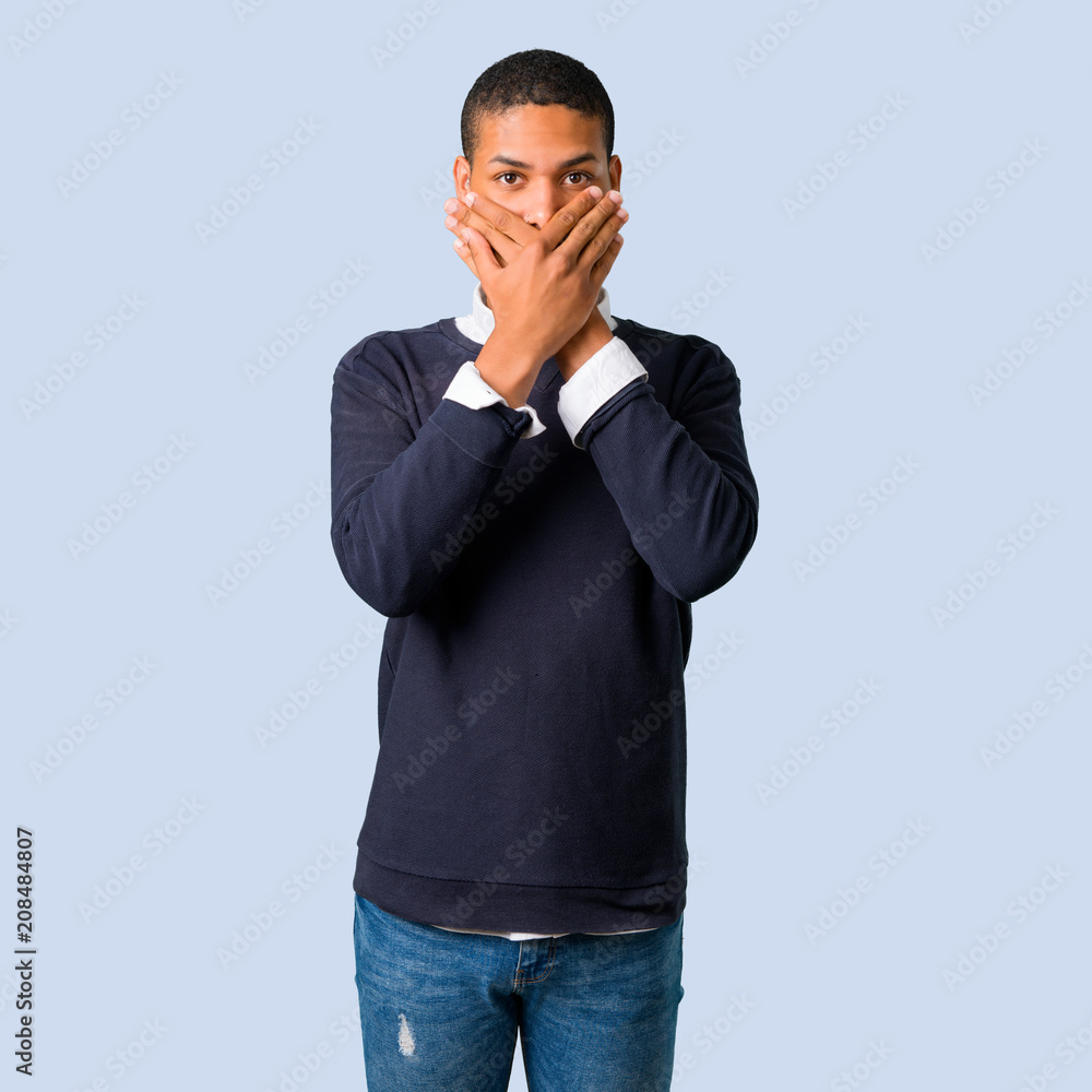 Young african american man covering mouth with hands on isolated blue background Young african american man covering mouth with hands on isolated blue background