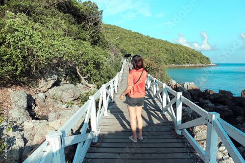 Woman standing on a wooden bridge taking a photo with a mobile With views of the sea and mountains.
