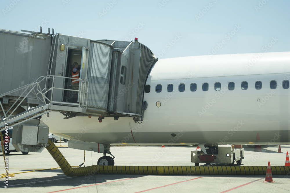 Obraz premium Modern passenger airplane parked to terminal building gate at airside apron of airport with airplane parts jet engine wing windows gear noon sun view air travel panoramic aerial background