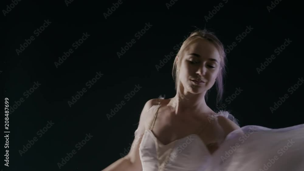 graceful sensual ballerina in white tutu dress dancing elements of classical or modern ballet in the dark with light and smoke on the black background, slow motion graceful sensual ballerina in white tutu dress dancing elements of classical or modern ballet in the dark with light and smoke on the black background, slow motion