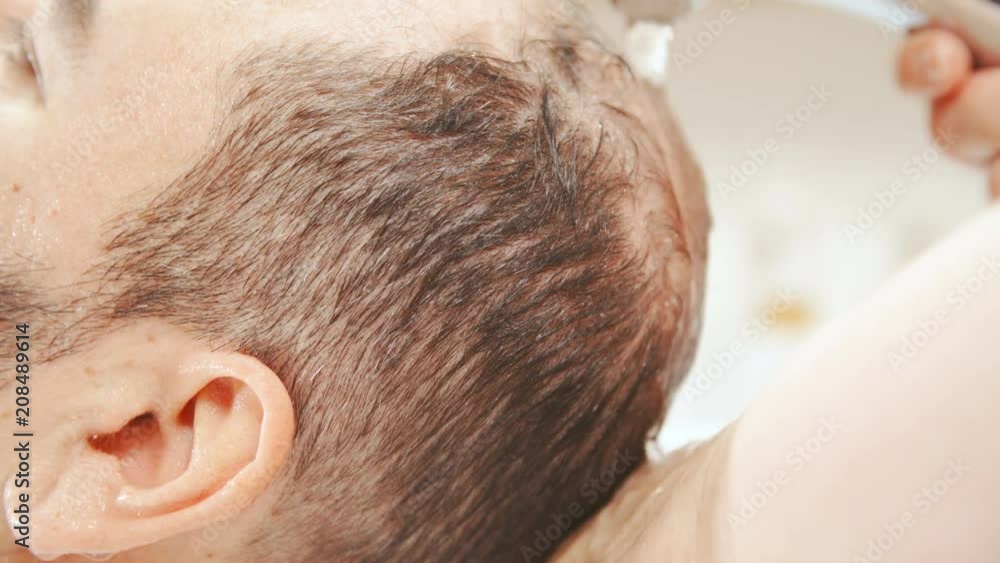 Pouring water over person hair to wash out shampoo close-up slow 4K. Close-up static shot slow motion of male person hair in focus with water running through hair while washing at hairdresser salon. Pouring water over person hair to wash out shampoo close-up slow 4K. Close-up static shot slow motion of male person hair in focus with water running through hair while washing at hairdresser salon.