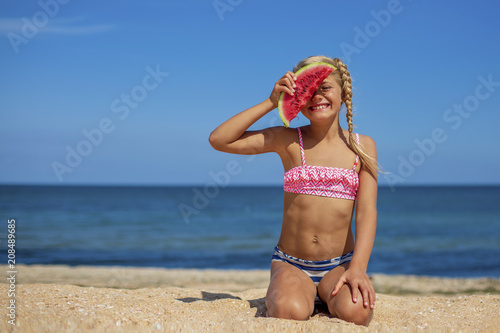 Portrait of pretty blonde little girl in swimsuit eating watermelon on  sandy beach near the sea in sunny day. Vacation. Healthy eating. Sport and  recreation Stock Photo | Adobe Stock