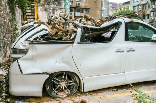 Broken white vehicle buried with old gray bricks from shattered wall. Insurance concept. 