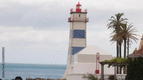Red and white lighthouse by the sea with palm trees and trees