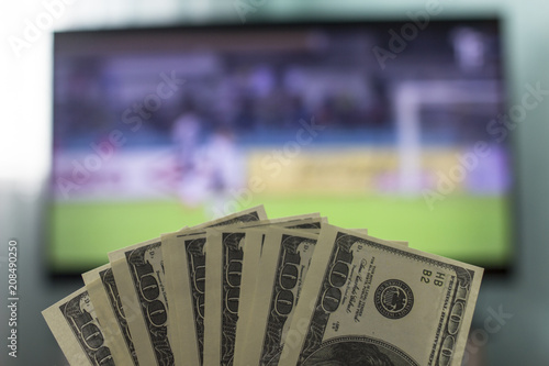 Canvas Print Men's hands keep money dollars against the background of a TV set on which footb