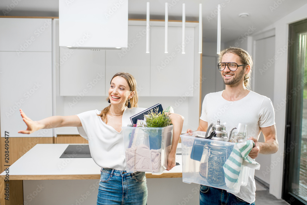 Young and happy couple holding boxes with different home stuff moving to a new modern house Young and happy couple holding boxes with different home stuff moving to a new modern house
