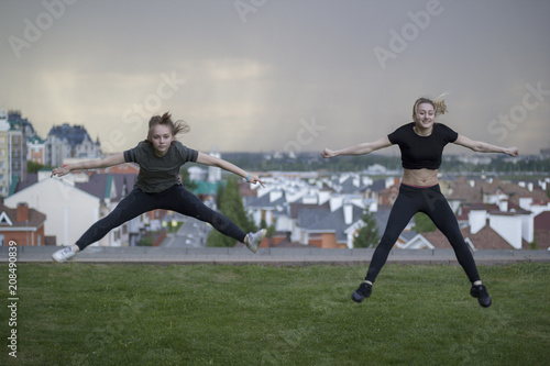 Two young female gymnasts doing acrobatics jumps with cityscape on background © KONSTANTIN SHISHKIN