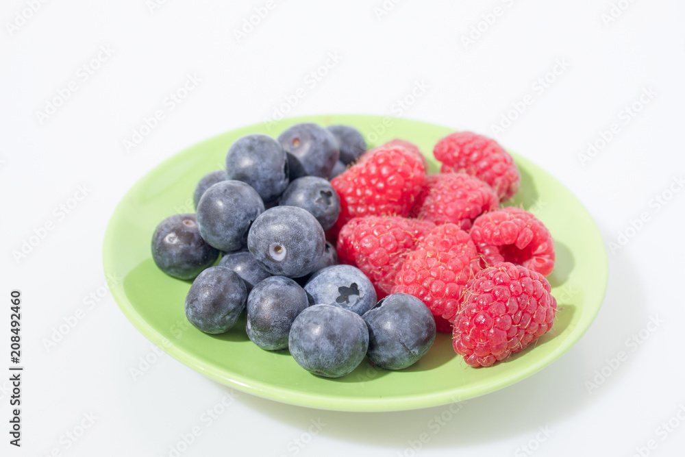 Fruit composition, blueberries and raspberries on a green plated isolated in a white background Fruit composition, blueberries and raspberries on a green plated isolated in a white background