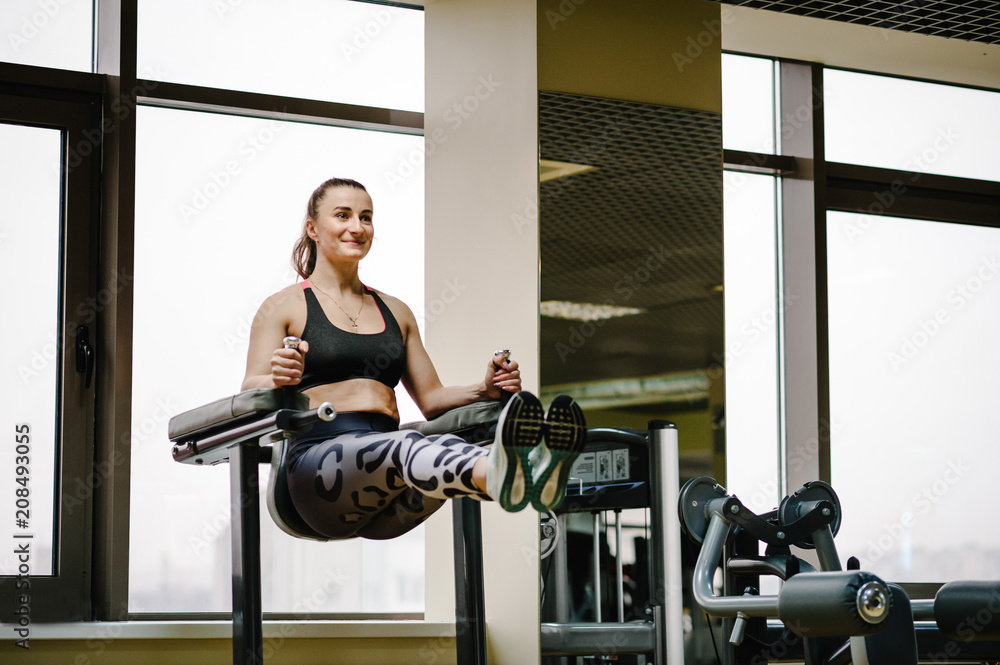 Fototapeta premium Portrait of sexy muscular girl wearing sportswear doing exercise on the bar raises his legs up, exercises on the press in the gym. Sport concept.