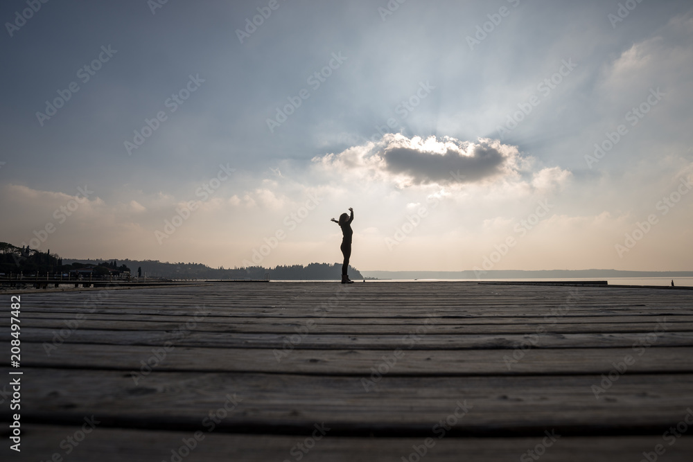 Side low angle view of a woman with arms outspread against cloudy sky