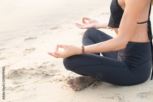Slim mature woman in black practicing yoga on sand beach